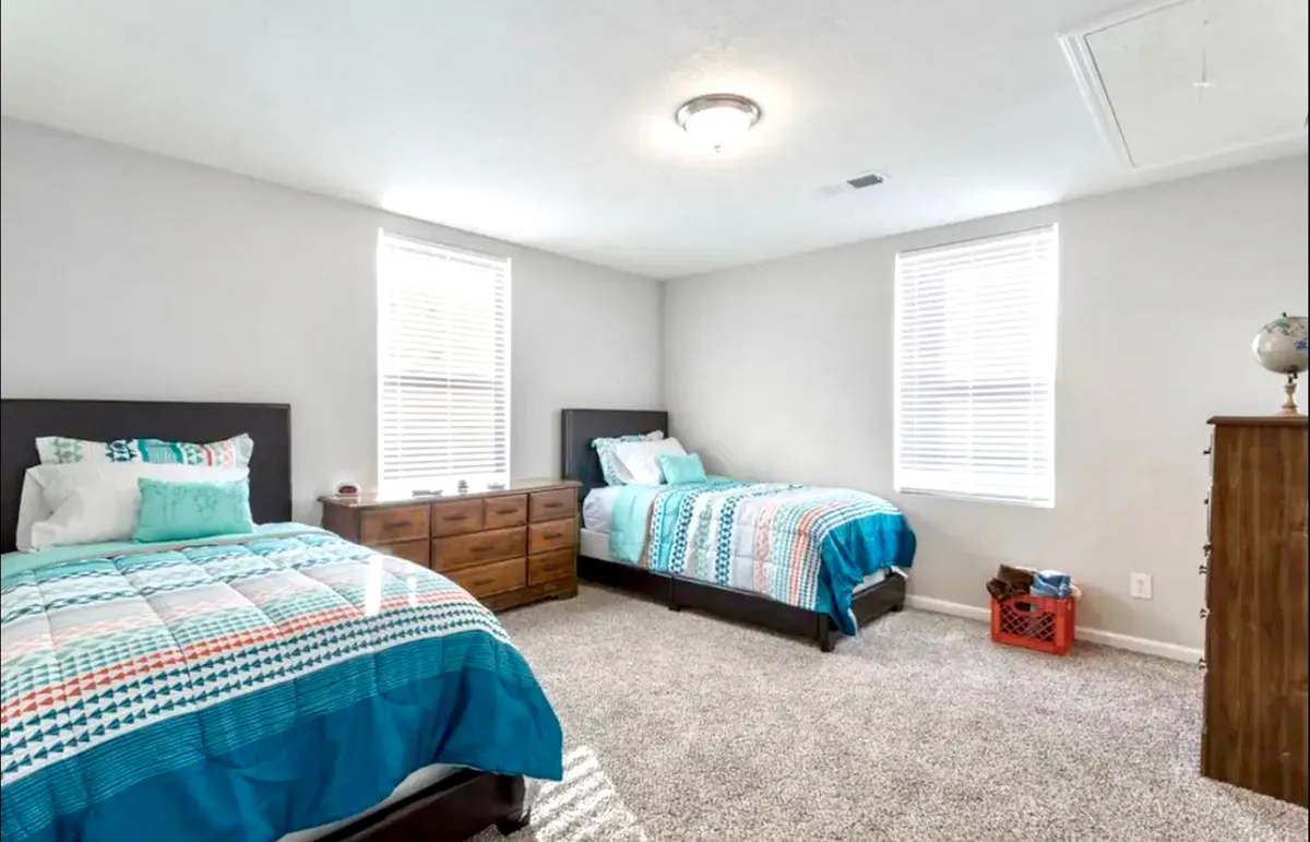 A comfortable bedroom with two beds, a dresser, and a decorative crate. The space is tidy and welcoming, ideal for families or friends traveling together. The decor is warm and functional, offering plenty of sleeping space and storage.