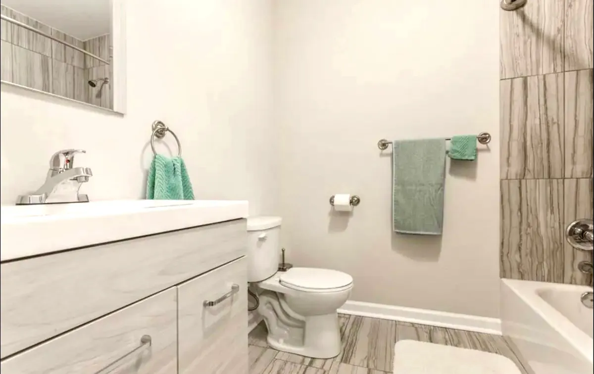 A modern bathroom featuring a vanity with sink, a bathtub, a toilet, and neatly folded towels. The space is bright and fresh, with clean lines and soothing colors, inviting guests to unwind after a long day.