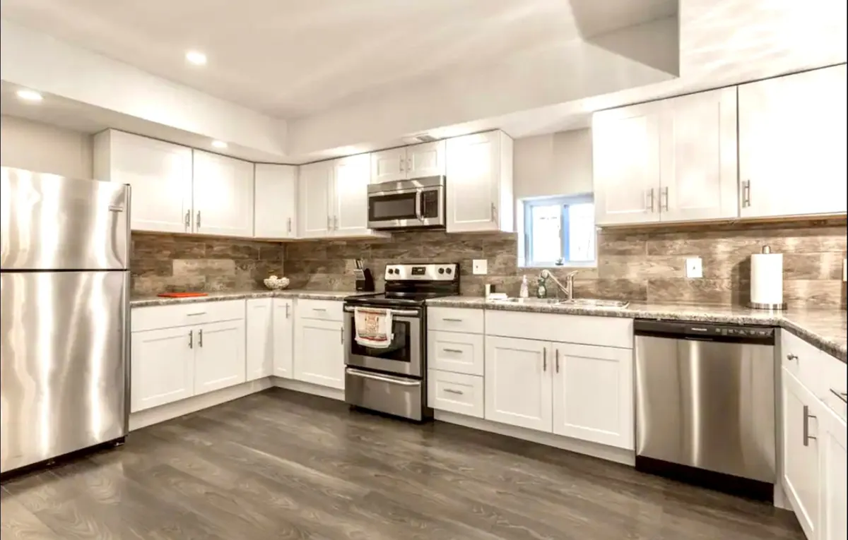 A modern kitchen with a stainless steel refrigerator, granite countertops, and a sleek stove and oven. Under-cabinet lighting creates a welcoming ambiance, and the space looks ideal for cooking family meals or gathering together after a day out.