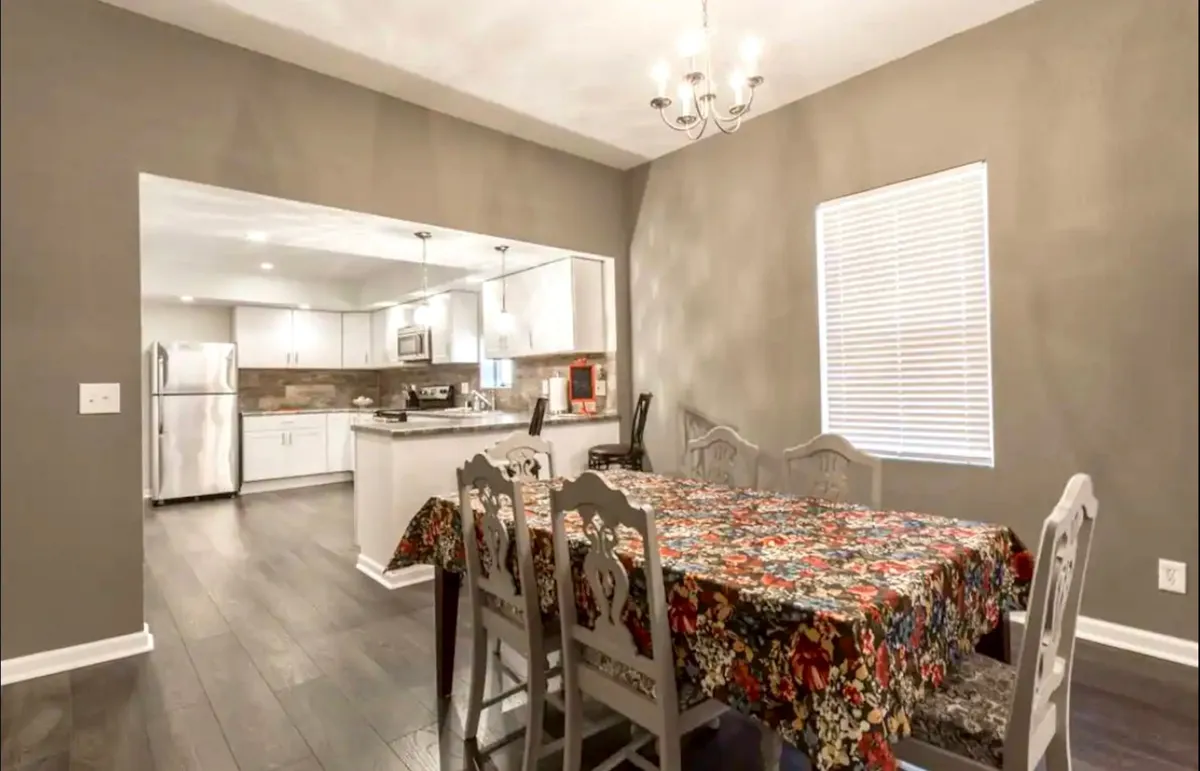 A charming dining table adorned with a floral tablecloth sits beneath a chandelier, with an open view into the kitchen. The scene is warm and homely, perfect for family dining, casual gatherings, and intimate conversations after a day of adventure.